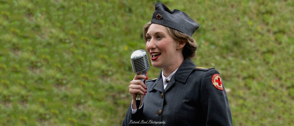 A female USO member singing passionately, her microphone in hand and a bright smile on her face. Dressed in a stylish performance outfit, she captivates her audience with her voice, embodying the spirit of entertainment and morale-boosting for troops during wartime.